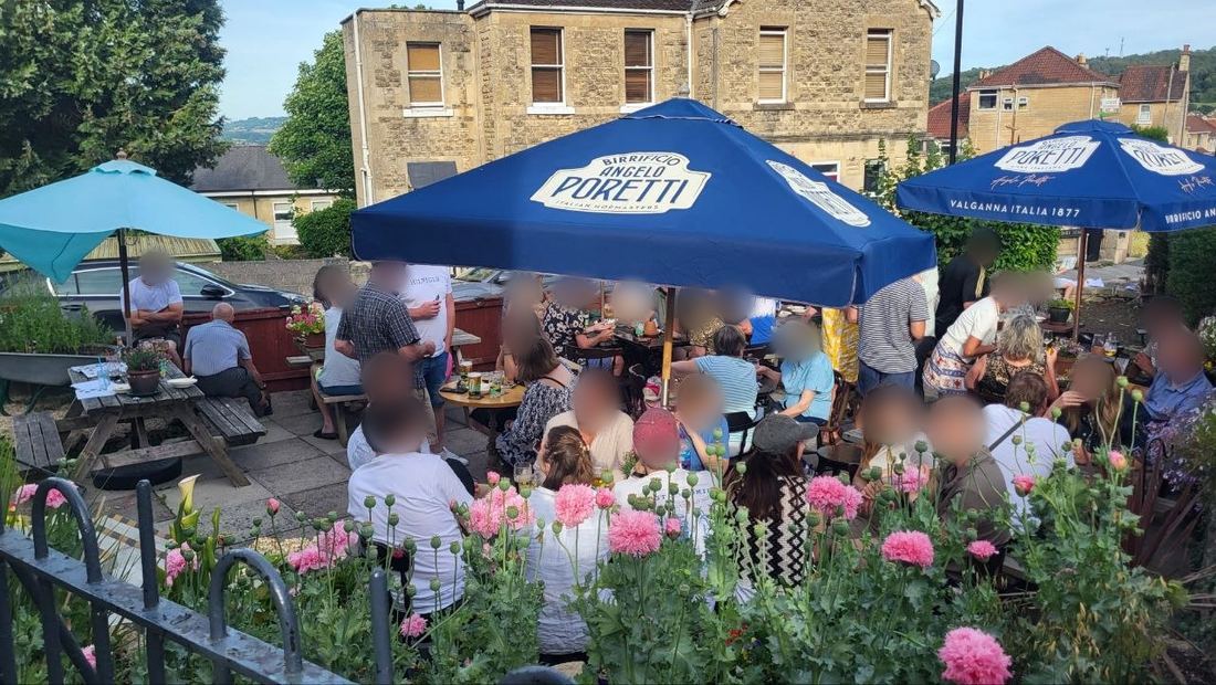 The beer garden full of people on a summer evening, with parasols and pink poppies.